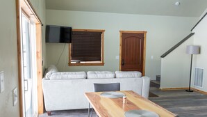 Un salon avec un canapé, une table en bois, un téléviseur fixé au mur et une porte.