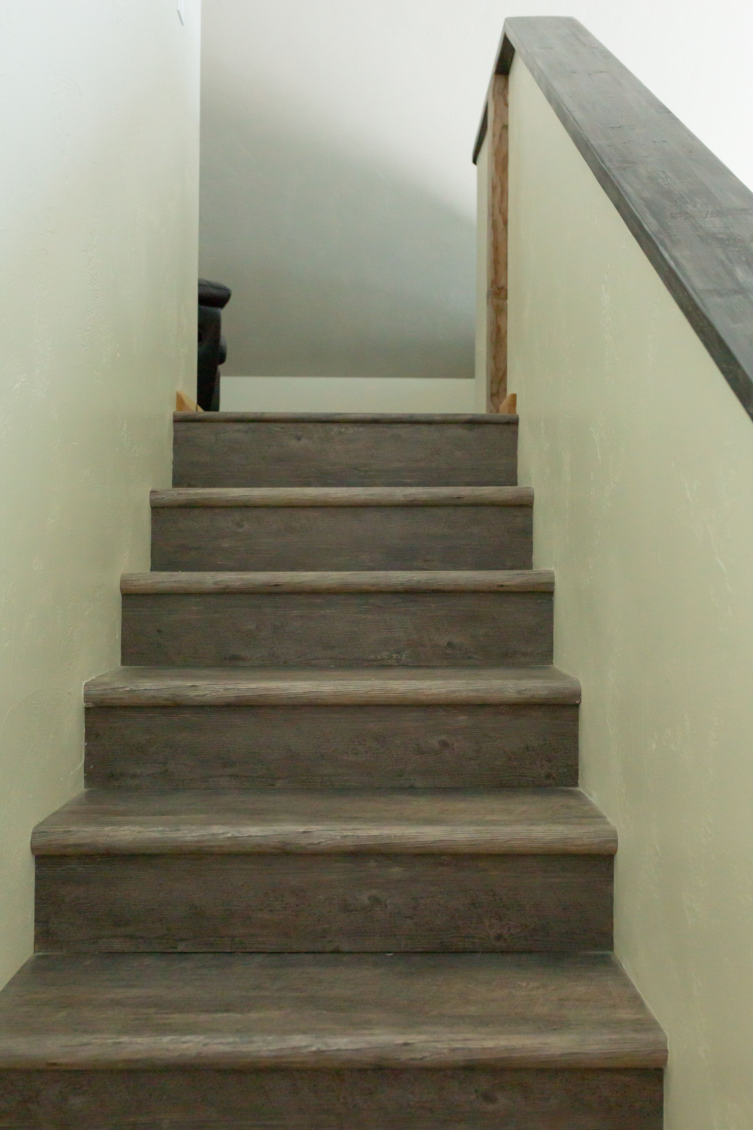 Eine Treppe mit Holzbodenstufen und einem dunklen Geländer, die zu einer Zwischenebene führt.