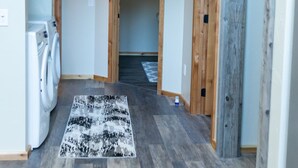 Un couloir avec un lave-linge, un tapis à motifs et des portes en bois.