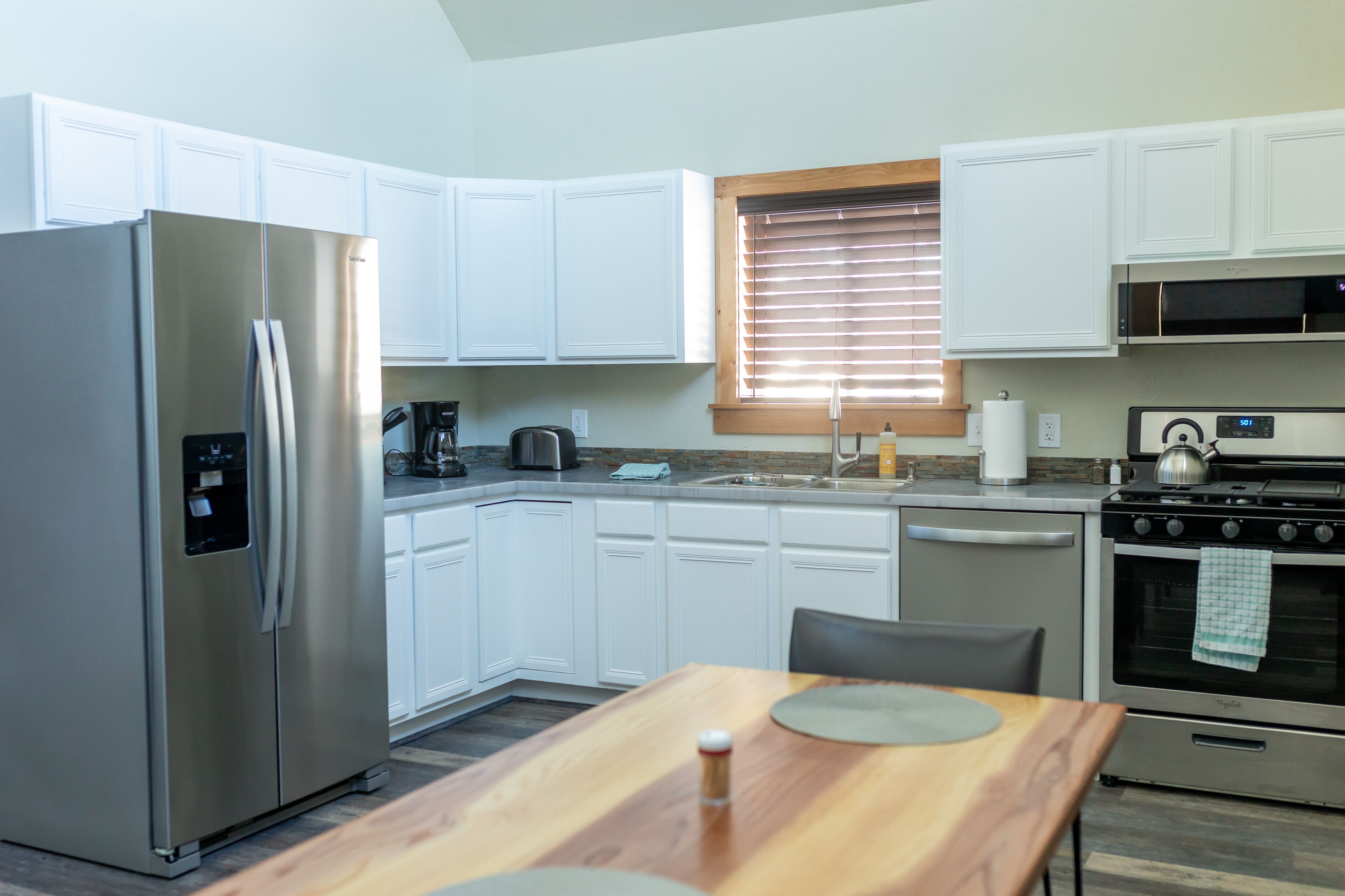 A compact kitchen with white cabinets, a stainless steel refrigerator, a microwave, a stove, and a dining table.