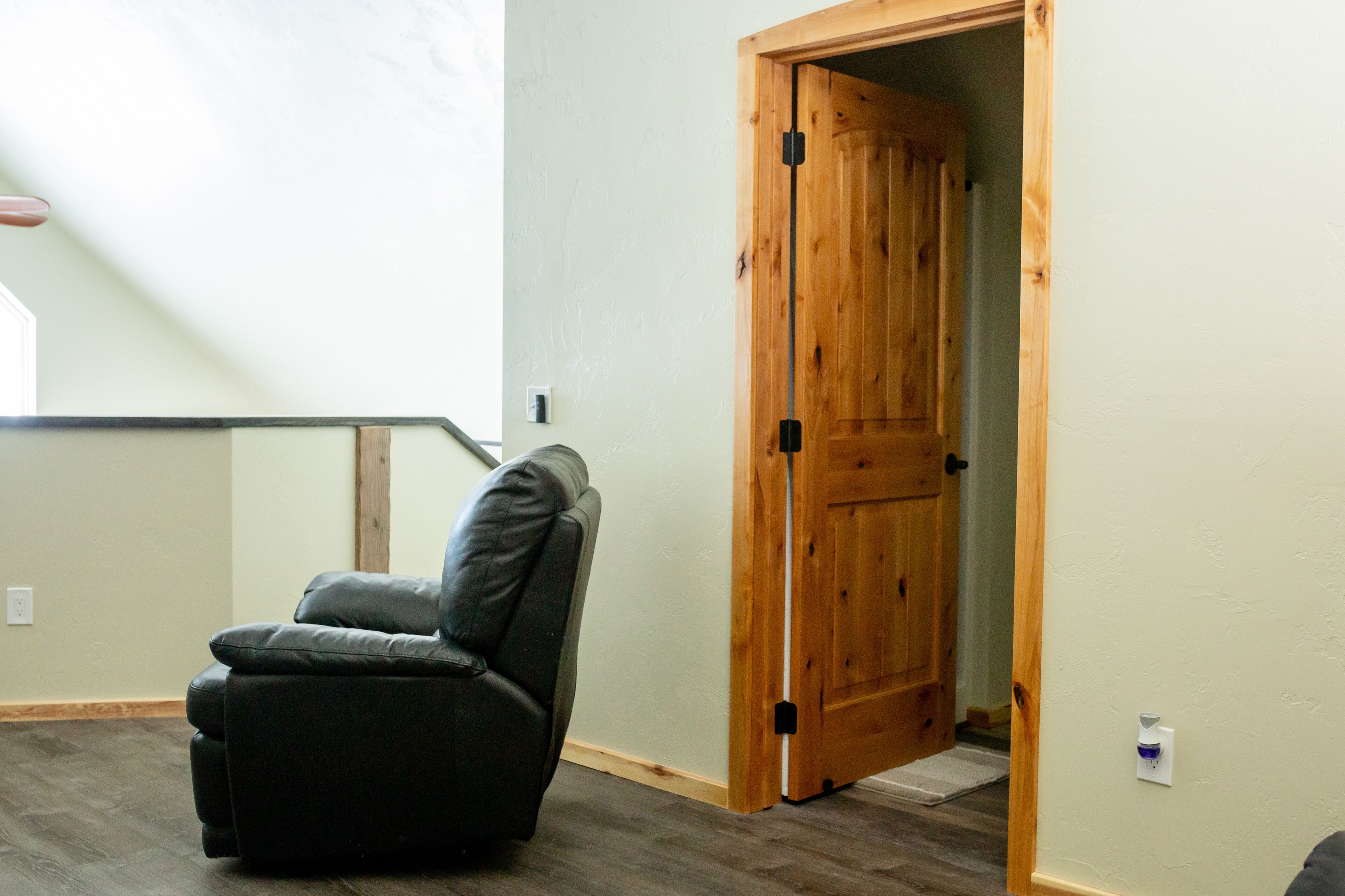 A room with a wooden door, a black leather chair, and a light-colored wall.