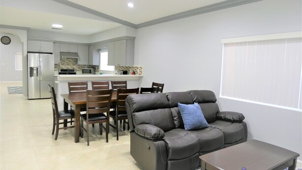 A modern living room with a leather sofa, dining table, and chairs. A kitchen with appliances and a window is visible in the background. - Spacious Home* 7 minutes to Disneyland (Anaheim)
