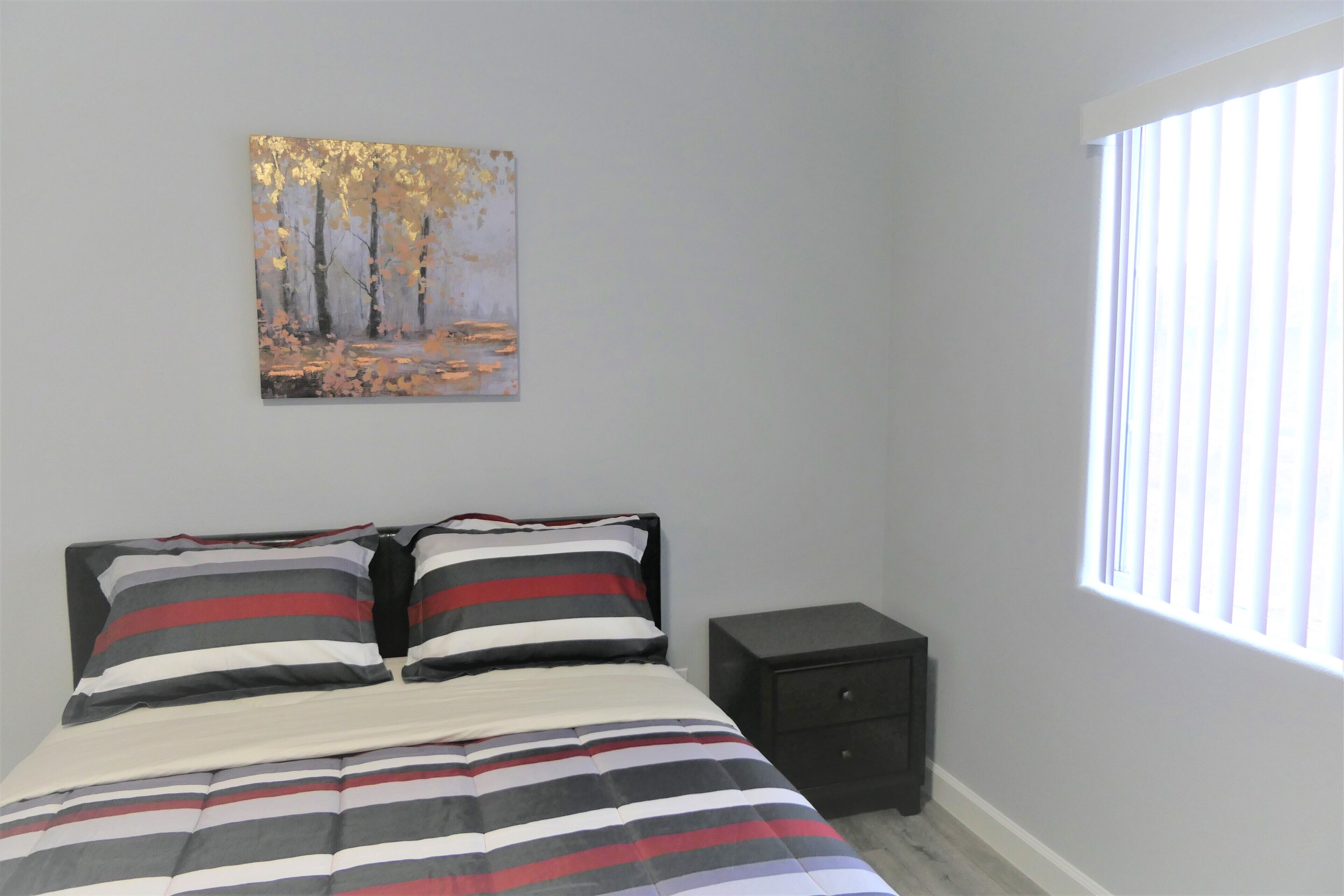 Une chambre à coucher avec un lit, une literie à rayures, une table de chevet, un tiroir et un tableau accroché au mur.