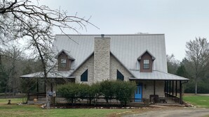 A two-story stone house with a metal roof, a blue door, and a porch with outdoor seating. - Landry Ranch Vacation Home - Close to the Franklin Ranch Baseball Complex! (Franklin)