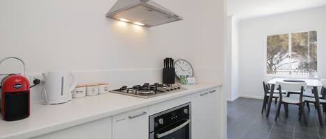 A modern kitchen with a gas stove, oven, and coffee maker. There is a dining area with a table and chairs.