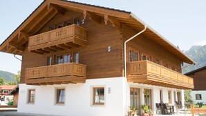 Ein zweistöckiges Holzhaus mit Balkonen und einer überdachten Terrasse, vor einer Bergkulisse.