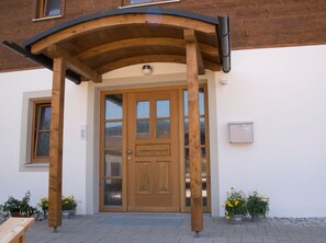 Une porte en bois avec des panneaux de verre, un porche en bois et des plantes en pot.
