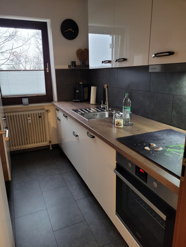 Eine moderne Küche mit Einbauofen, Spüle und Fenster mit Jalousien.