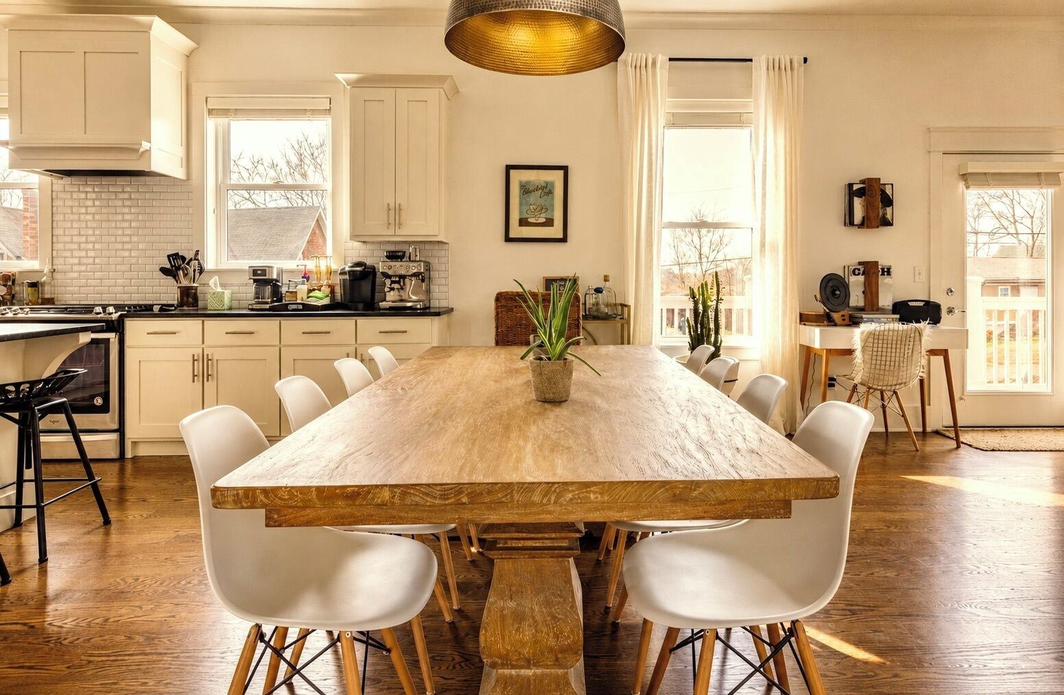 Une cuisine spacieuse avec des meubles blancs, une table à manger en bois entourée de chaises et une grande fenêtre qui laisse entrer la lumière naturelle.