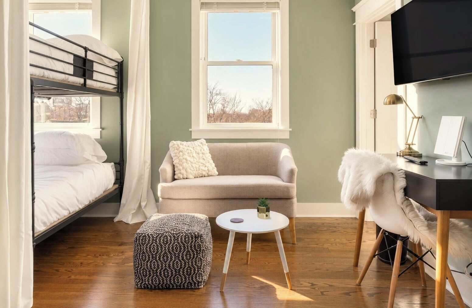 A room with a bunk bed, a sofa, a round coffee table, a desk with a computer, and a chair with a fur throw.