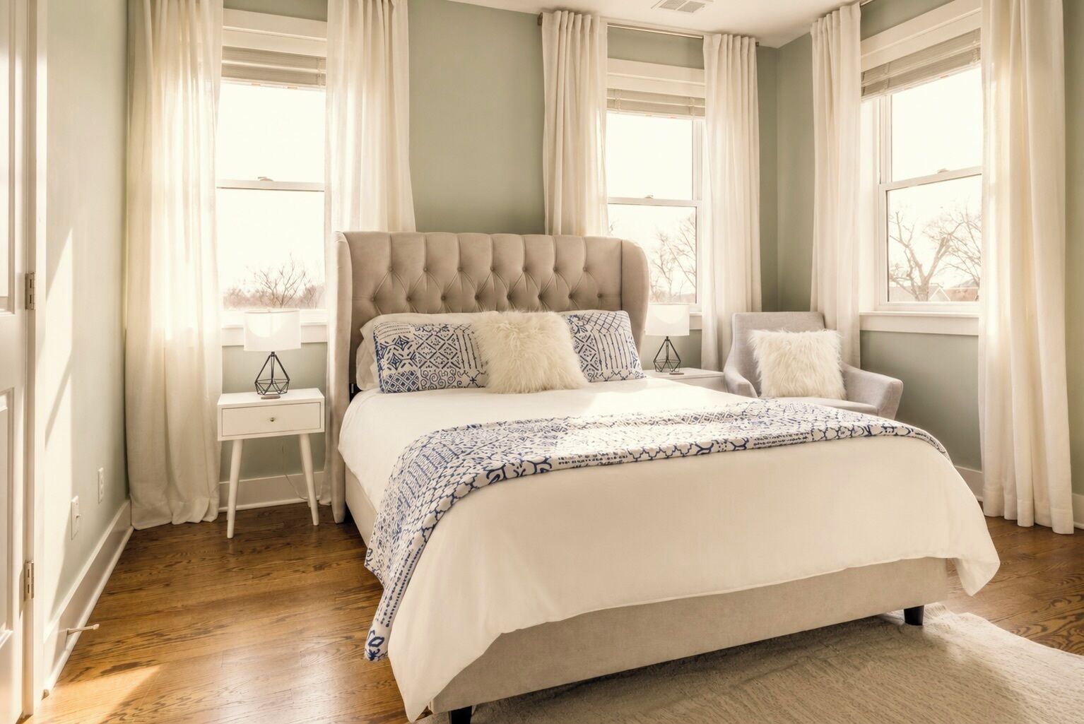 Une chambre à coucher avec un grand lit, une table de chevet, une chaise et une fenêtre avec des rideaux.