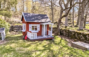 Situated in a wooded area, this charming house features a porch with white railings and a small entrance.