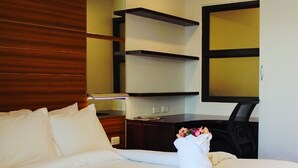 A neatly made bed with white linens, a wooden headboard, a desk with a chair, and a mirror on the wall.
