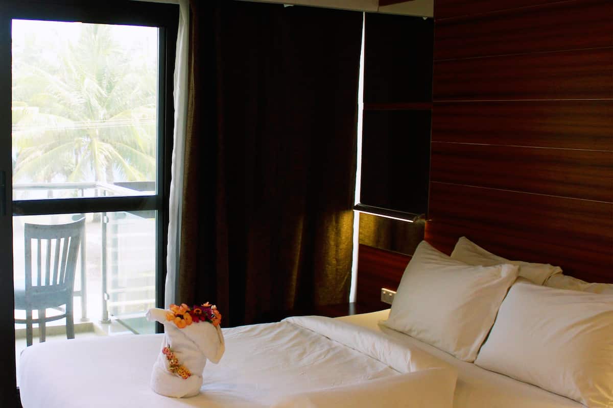 A hotel room with a bed, a chair, a window, and a view of palm trees.