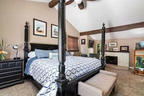 A bedroom with a four-poster bed, a fireplace, and framed artwork on the walls.