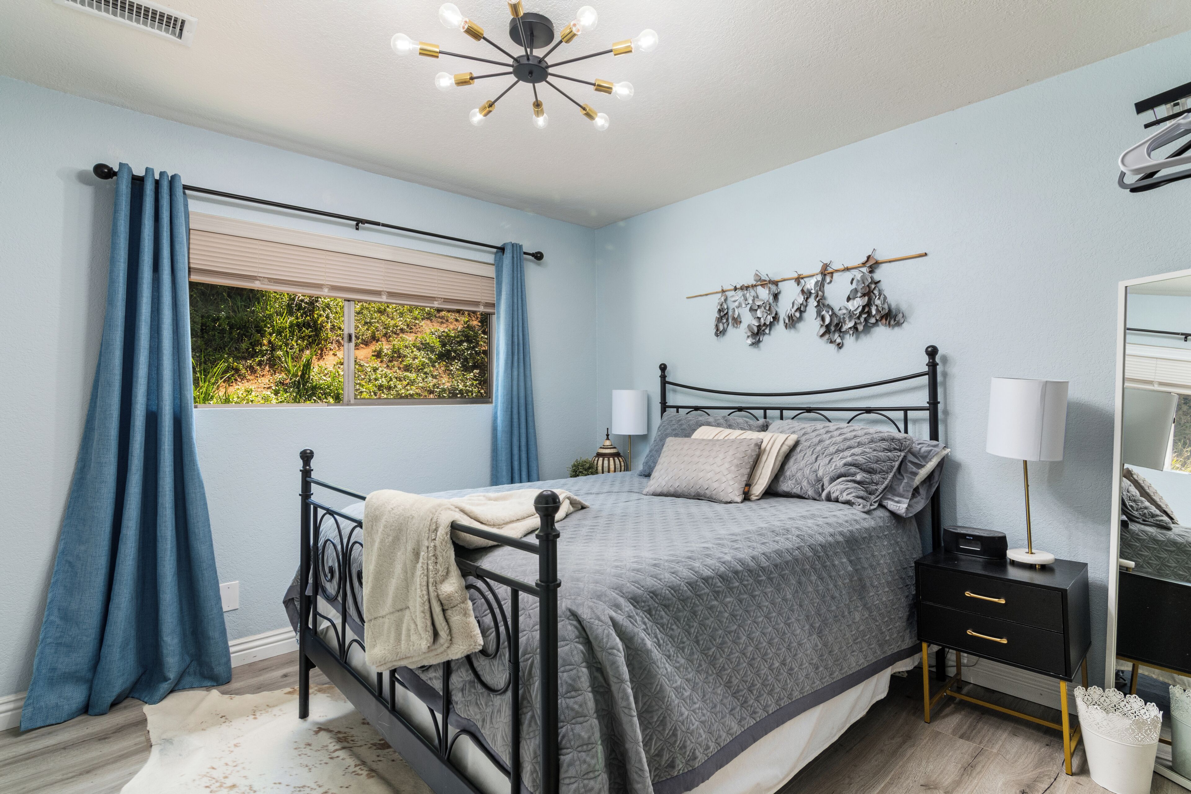 A bedroom with a bed, bedside table, lamp, and a wall-mounted mirror.