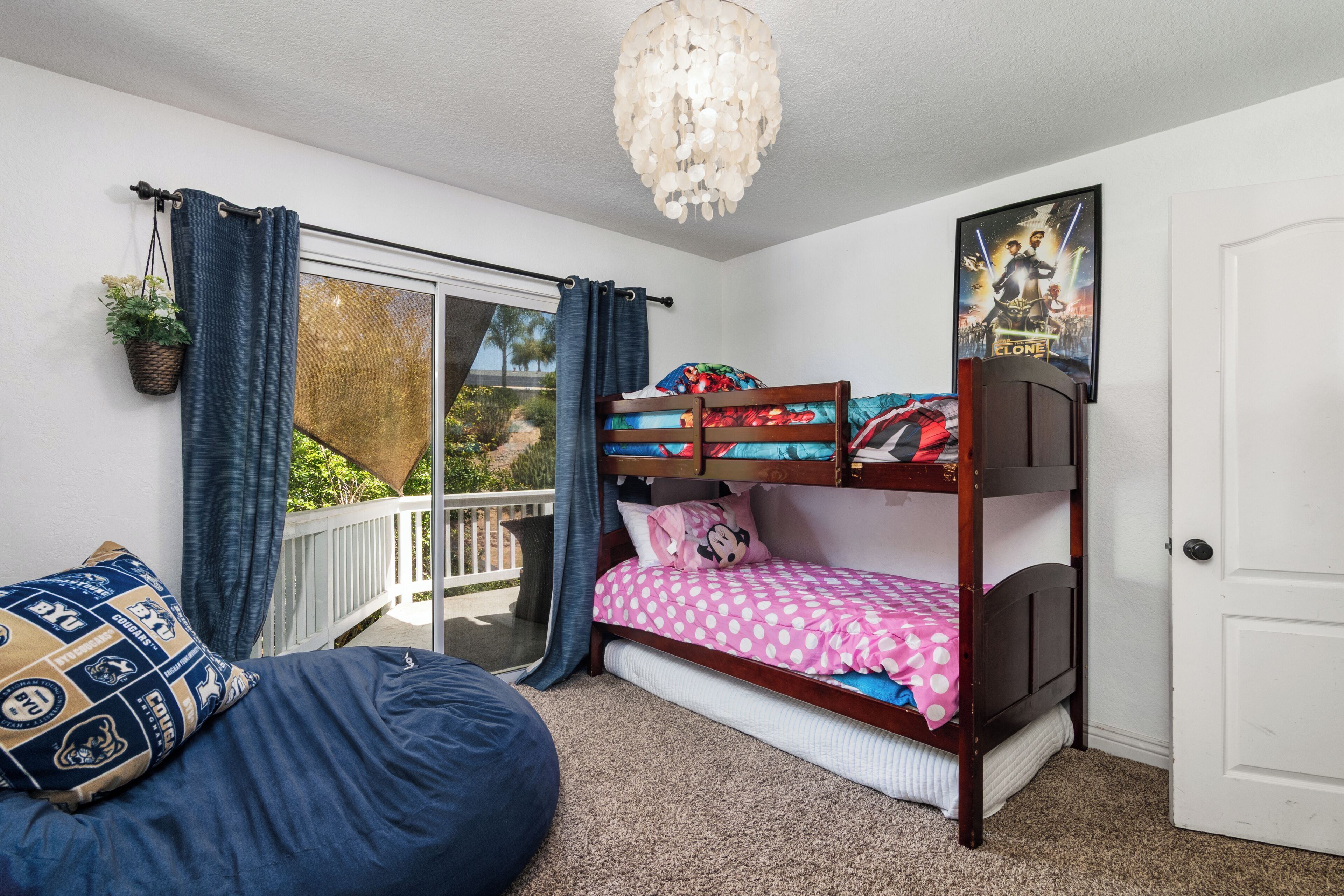 A bedroom with a bunk bed, a bean bag chair, a chandelier, and a poster on the wall.