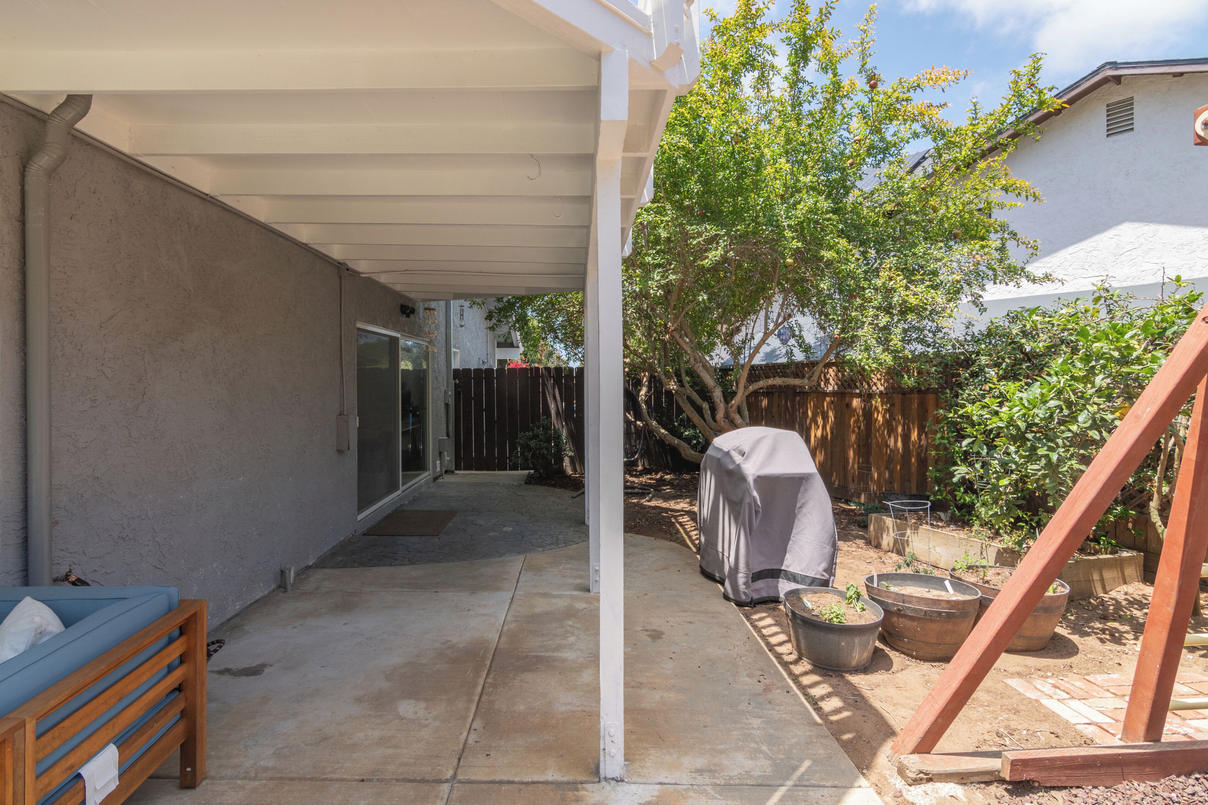 A covered patio area with a wooden bench, potted plants, and a grill.
