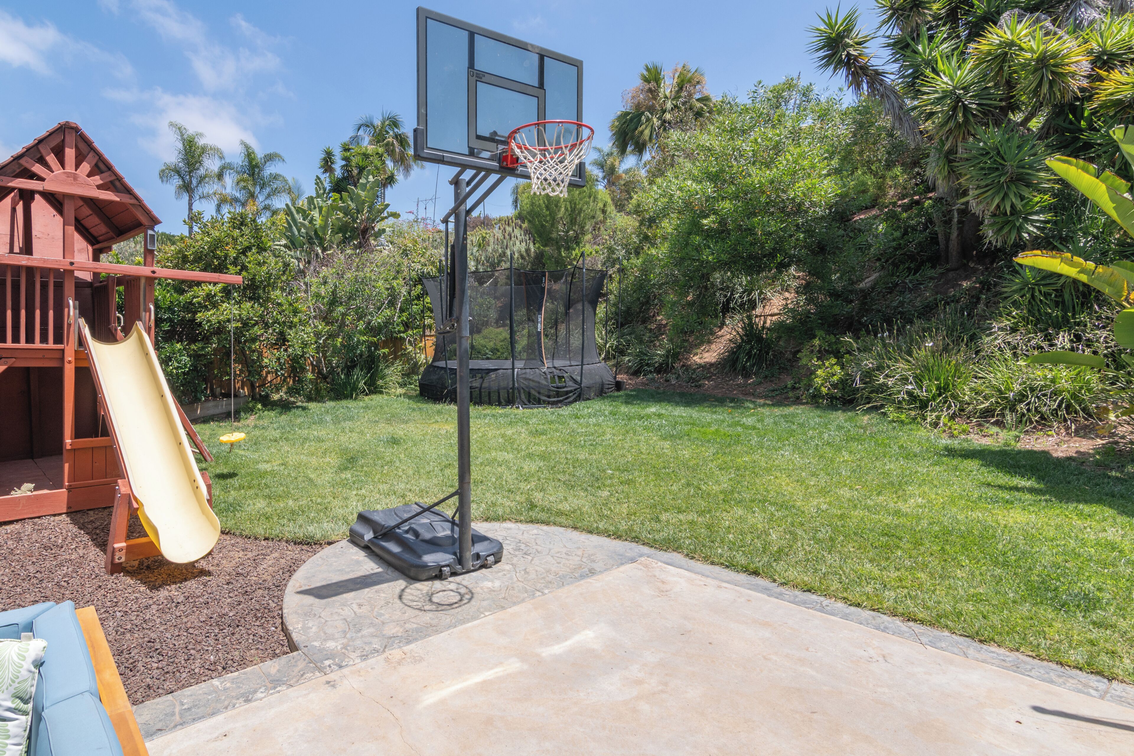 A basketball hoop, a slide, and a wooden play structure in a backyard.