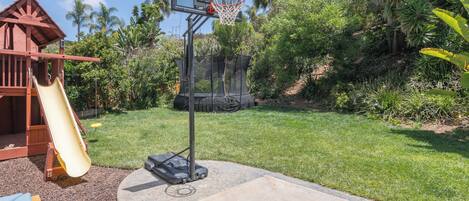 A basketball hoop, a slide, and a wooden play structure in a backyard.