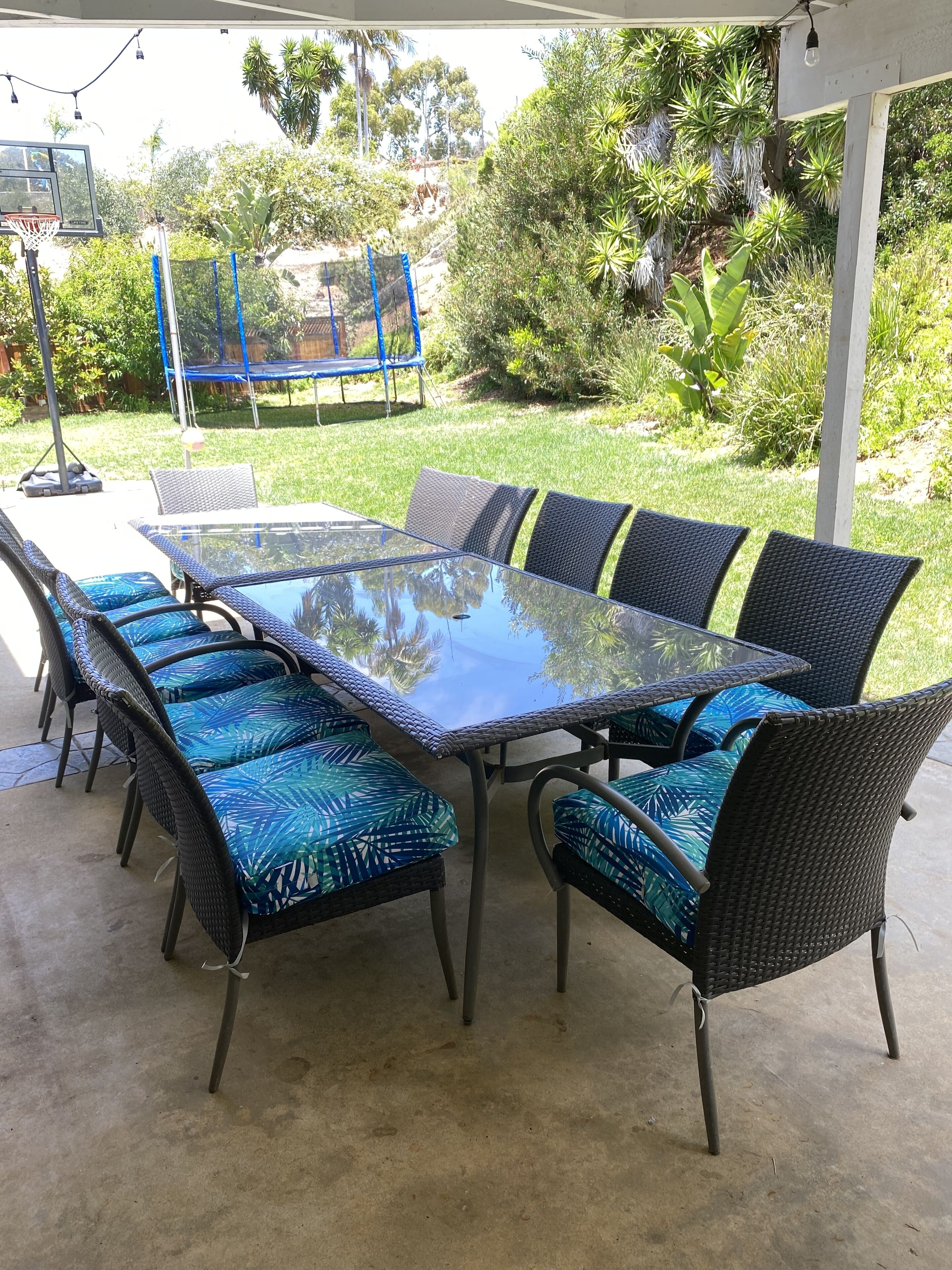 Une terrasse extérieure avec une table à plateau de verre, entourée de chaises en osier dotées de coussins bleus.