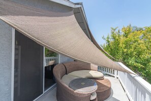 A balcony with a wicker sofa, a glass table, and a large shade sail.