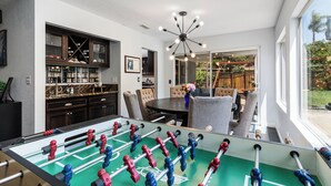 Un soggiorno moderno con tavolo da calcio, zona pranzo con tavolo rotondo e un'ampia finestra vista all'esterno.
