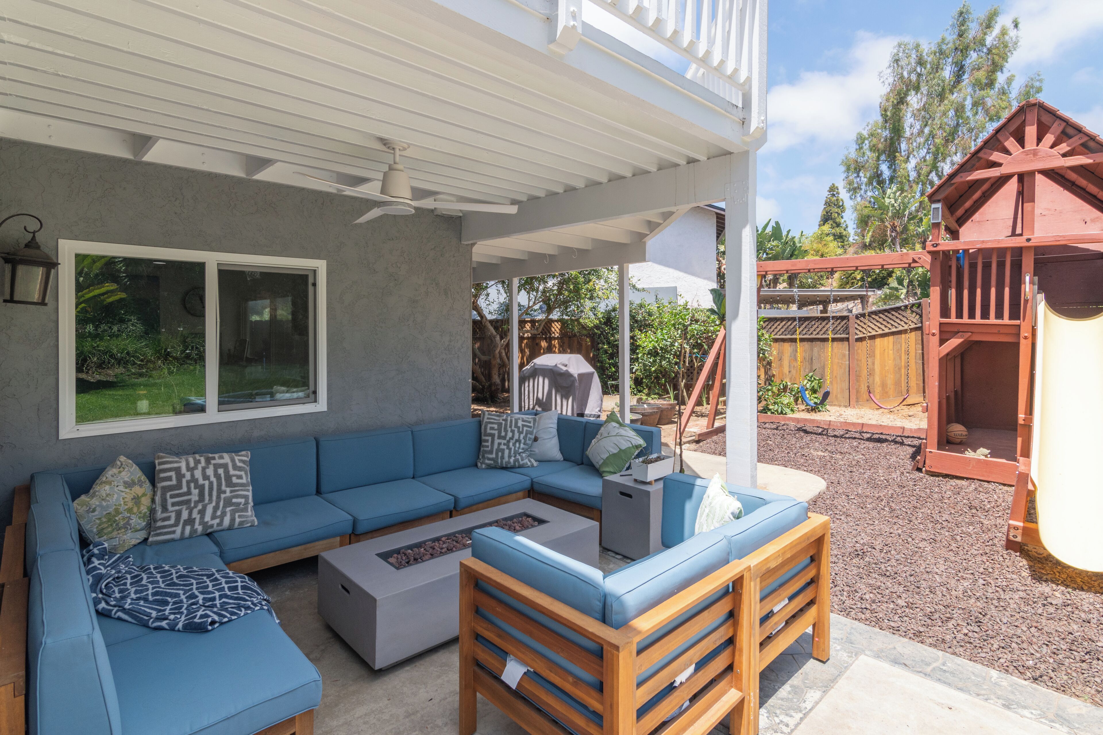 A covered patio with a sectional sofa, a wooden bench, and a play structure in the background.