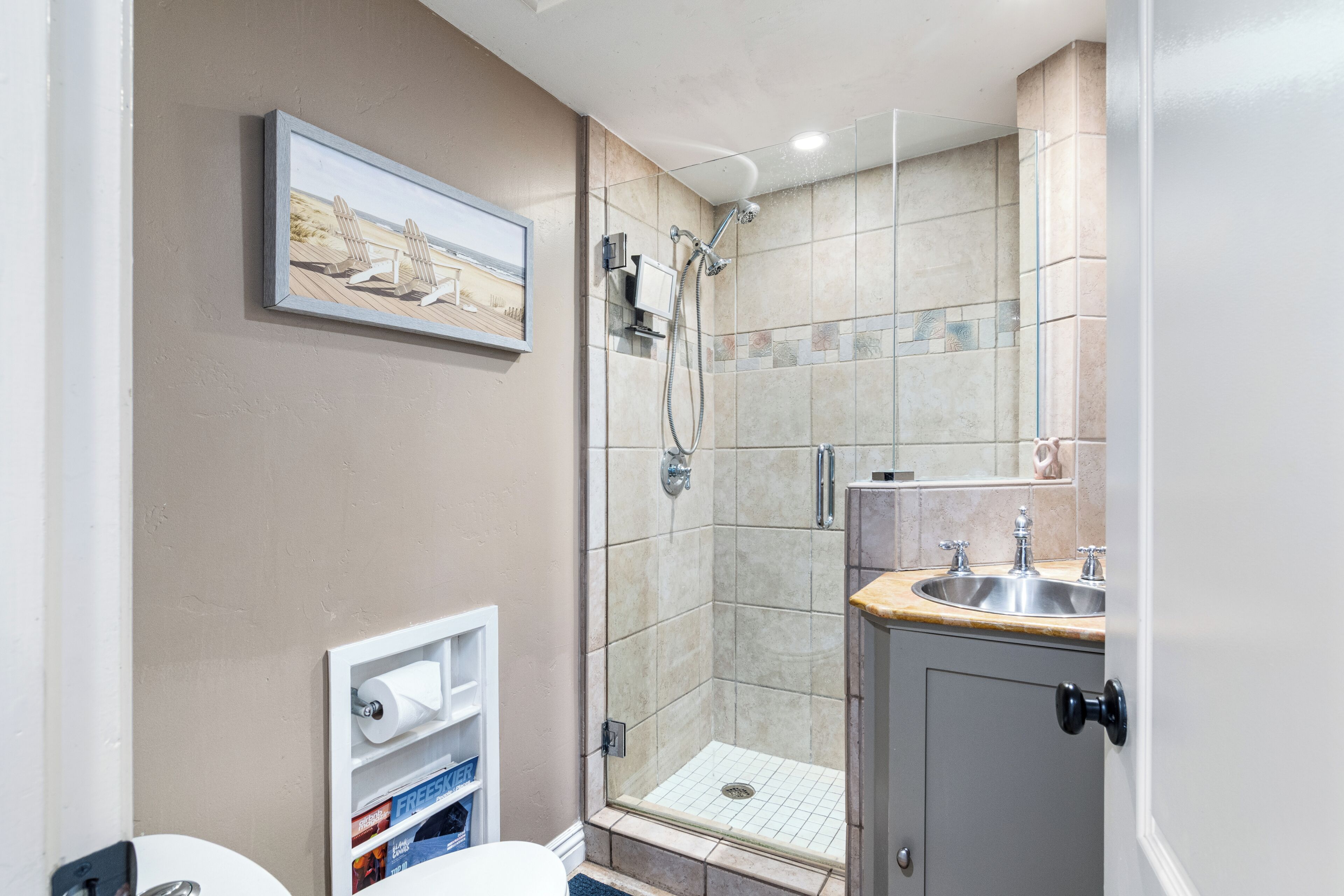 A bathroom with a shower, sink, toilet, and a framed picture on the wall.