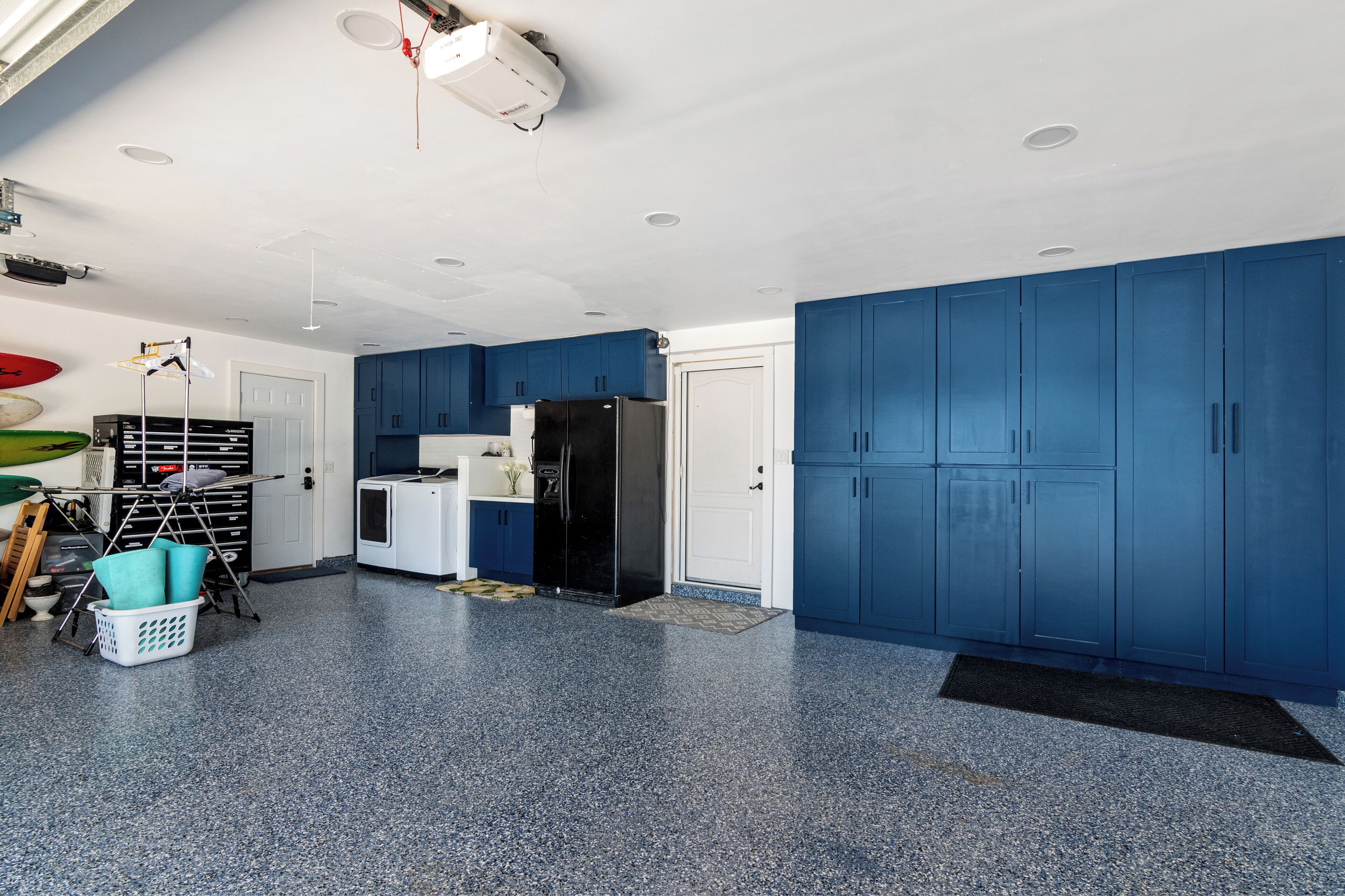 A spacious kitchen with blue cabinets, a black refrigerator, and a ceiling-mounted projector.