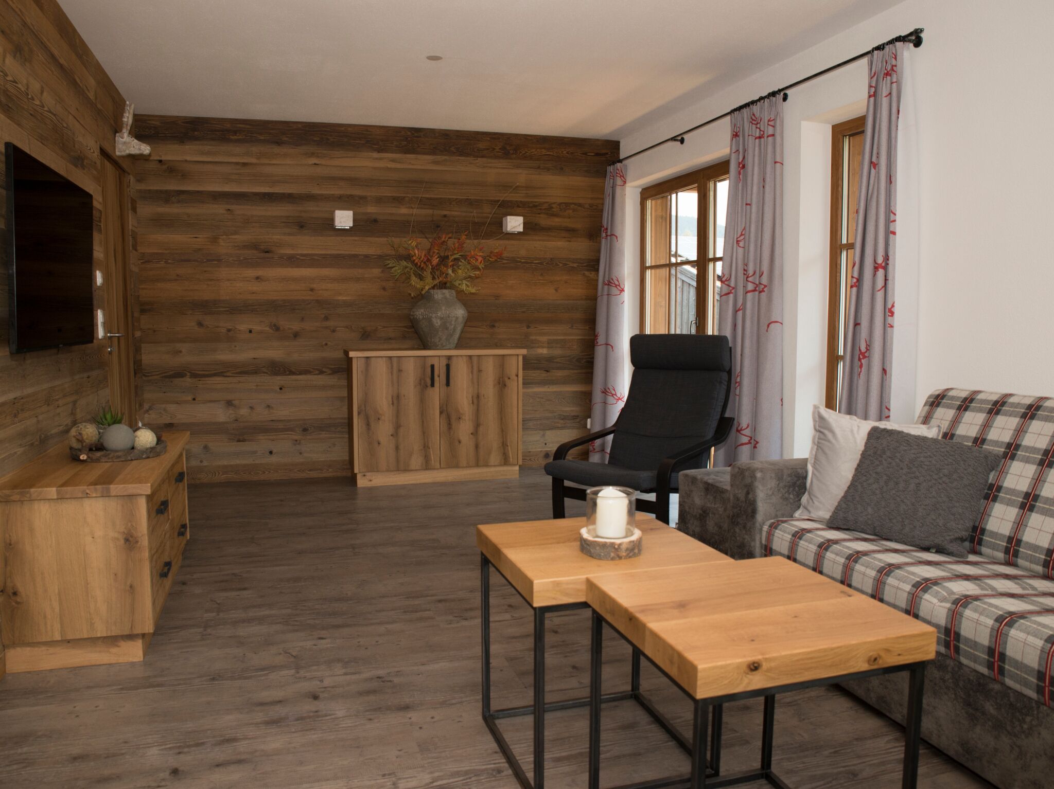 Ein gemütliches Zimmer mit Holzwänden, einem Holzschrank, einem schwarzen Stuhl, einem karierten Sofa und einem Holztisch mit Kerze.