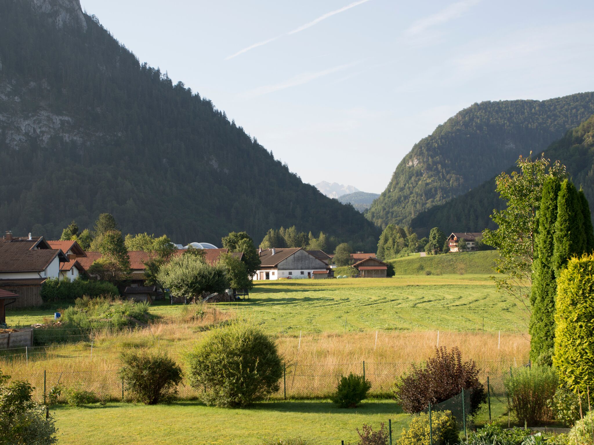 Een landelijk landschap met huizen, een omheind veld en bergen op de achtergrond.
