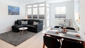 En moderne stue med en sort sofa, et lille rundt bord og et spiseområde med et hvidt bord og stole.