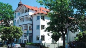 En bygning med flere etager, rødt tag og hvide vægge, med en balkon på anden sal.