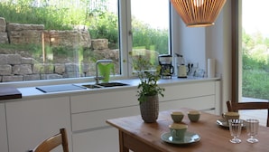 A kitchen with a stone wall, a sink, a coffee maker, and a dining table with cups and glasses. - Dream vacation in the Allgäu in the eco house with a clear view of nature (Isny)