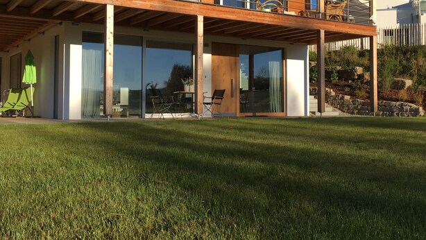 A modern two-story house with a wooden deck, sliding glass doors, and outdoor seating. - Dream vacation in the Allgäu in the eco house with a clear view of nature (Isny)