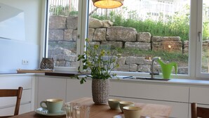 A dining area with a wooden table, a vase with flowers, and a stone wall outside. - Dream vacation in the Allgäu in the eco house with a clear view of nature (Isny)