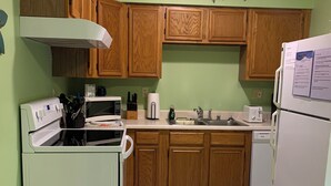 A compact kitchen with wooden cabinets, a white refrigerator, a microwave, and a stove.