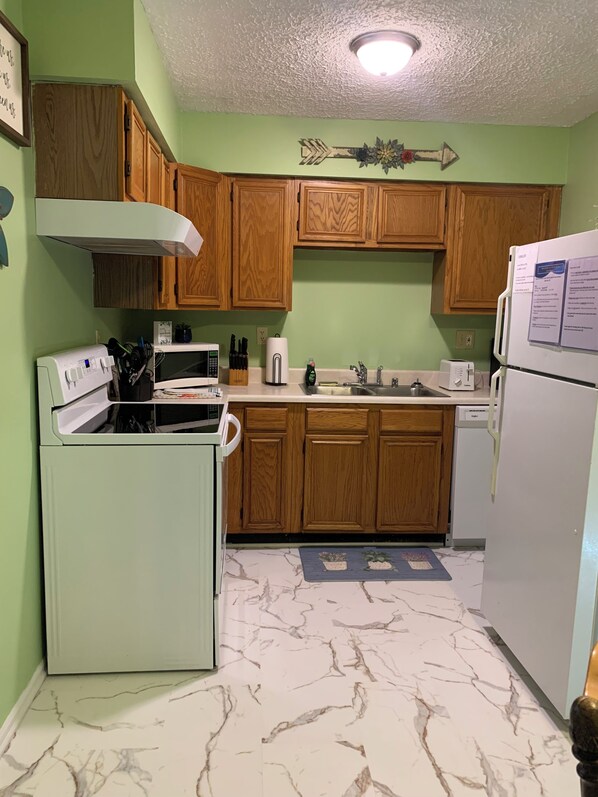 A compact kitchen with wooden cabinets, a white refrigerator, a microwave, and a stove.