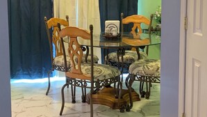 A dining area with a glass table and four chairs, a coffee maker, and a vase with flowers.