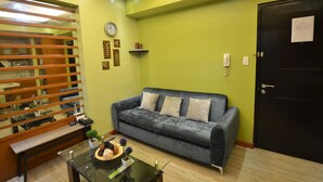A living room with a grey sofa, a glass coffee table, a wooden bench, and a black door. - A Homey Place Manila, 1 Bedroom (Manila)