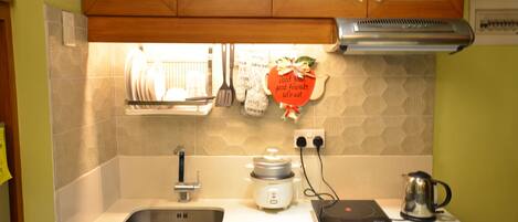 A kitchen with a sink, a rice cooker, a kettle, and a wall-mounted spice rack.