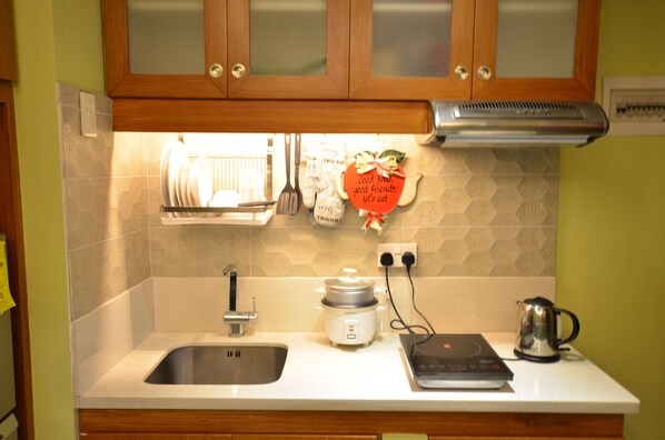 A kitchen with a sink, a rice cooker, a kettle, and a wall-mounted spice rack.