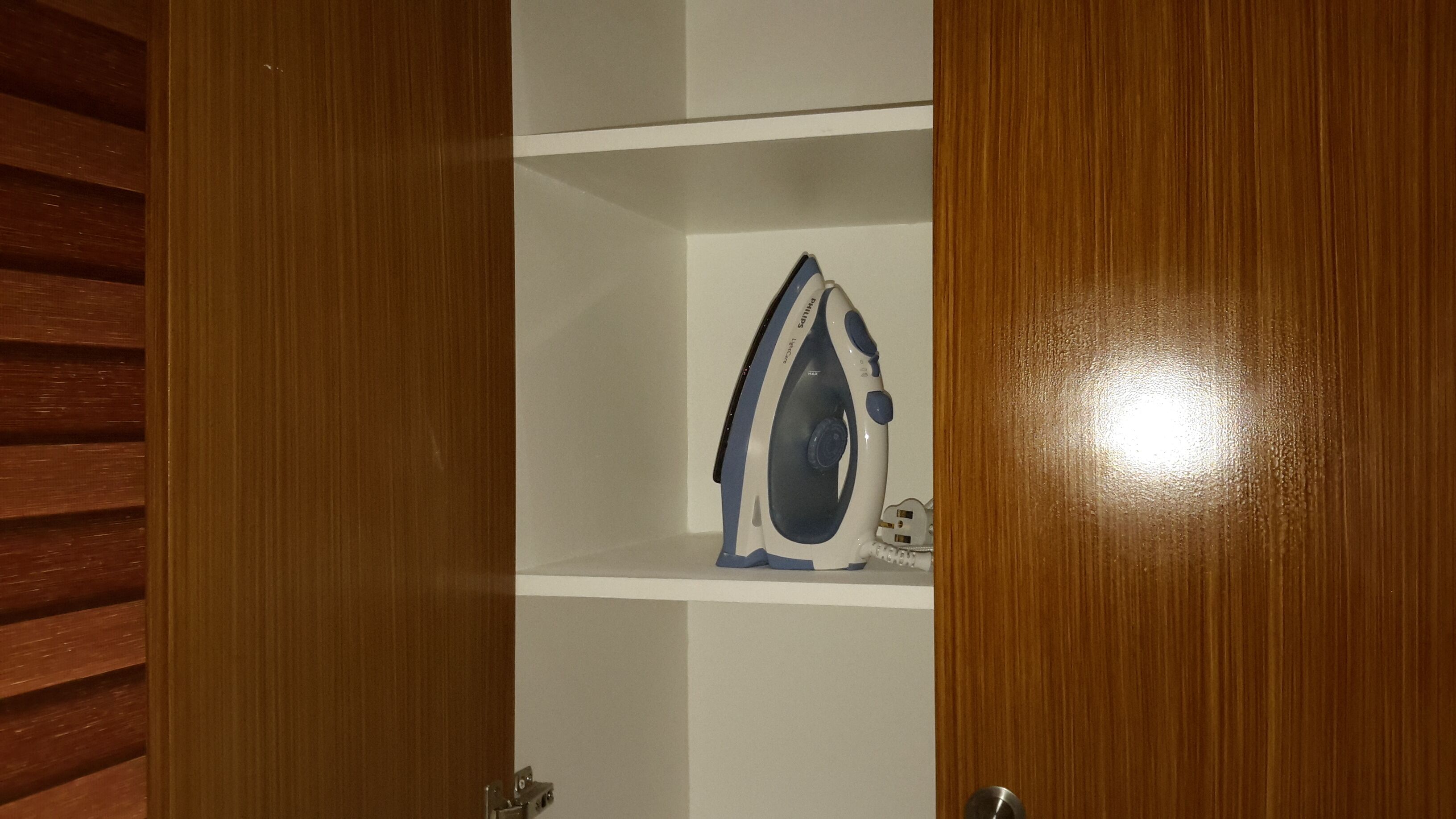 A wooden wardrobe with a white interior and a single blue and white iron placed inside.