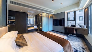 A modern hotel room with a large bed, a desk, a TV, and a view of the city.