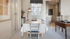 A dining area with a table set for four, a lamp, and a view of the kitchen. - Notting Hill Newly Decorated 3-Bedrooms with large Private Garden (London)