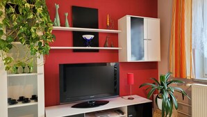 Moderni olohuone, jossa on punainen tehosteseinä, litteänäyttöinen televisio, valkoiset hyllyt ja koriste-esineitä.