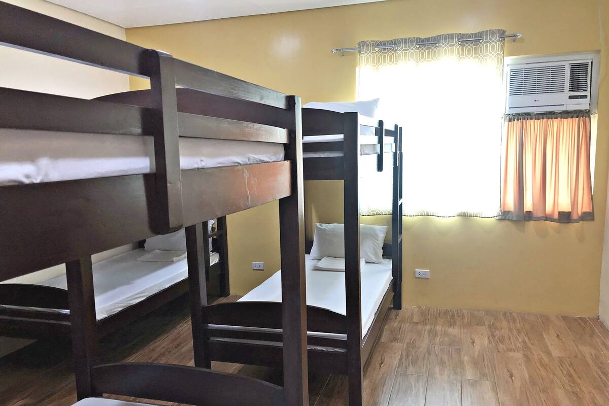 Une chambre de dortoir avec des lits superposés, une fenêtre avec des rideaux et un appareil de climatisation.
