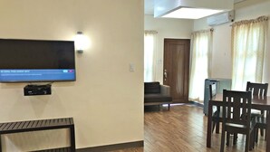Uma sala de estar com televisão de tela plana na parede, um banco de madeira, um sofá e um espaço de jantar com mesa e cadeiras.