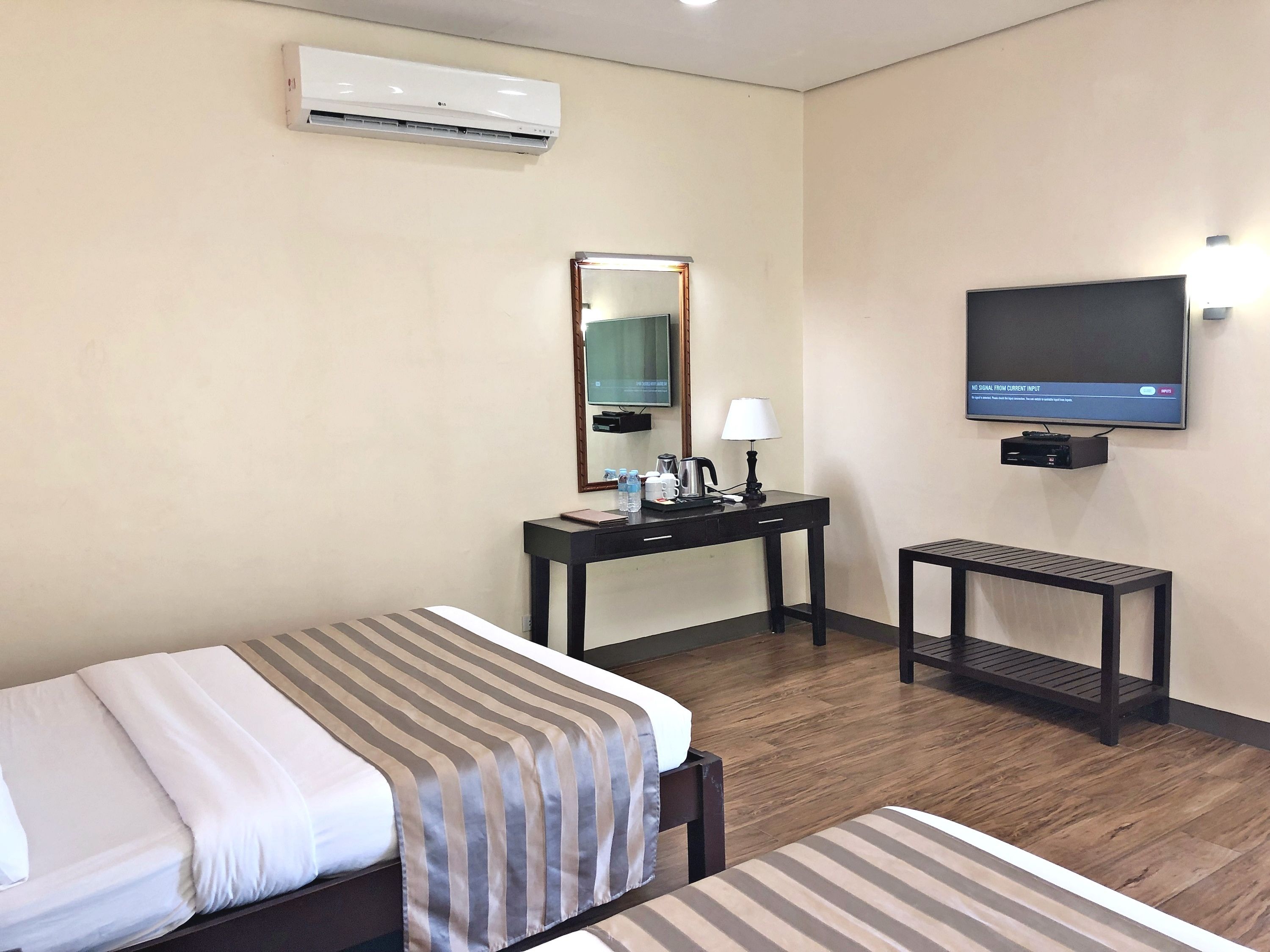 A hotel room with a bed, a desk with a lamp, a television, and an air conditioning unit.